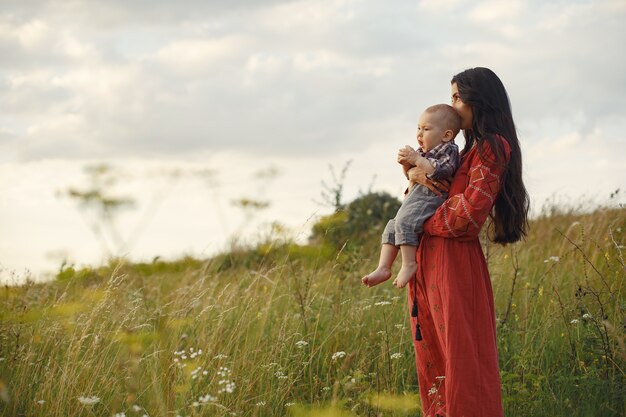 Familia en un campo de verano. Madre con un vestido rojo. Niño lindo.