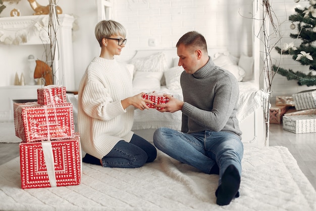 Familia en casa. Pareja cerca de adornos navideños. Mujer con un suéter gris.