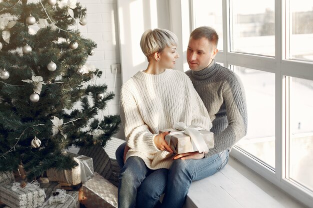 Familia en casa. Pareja cerca de adornos navideños. Mujer con un suéter gris.