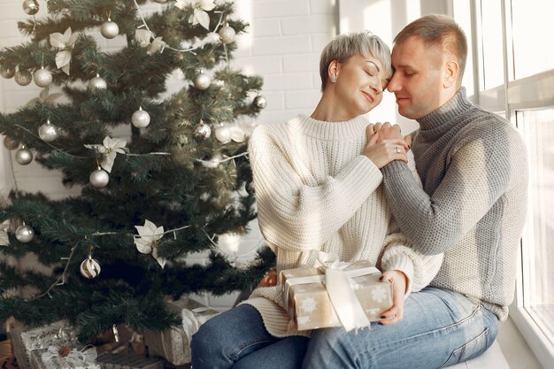 Familia en casa. Pareja cerca de adornos navideños. Mujer con un suéter gris.