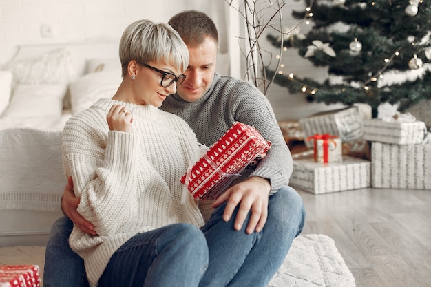 Familia en casa. Pareja cerca de adornos navideños. Mujer con un suéter gris.