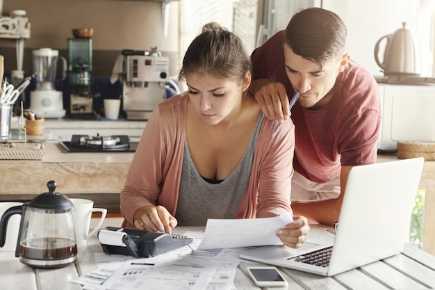 Familia caucásica joven que enfrenta un problema de deuda de crédito. Hermosa mujer sosteniendo trozo de papel y calculando las finanzas