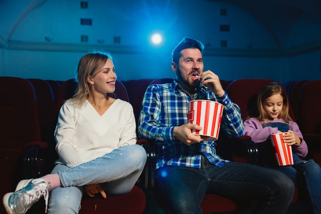 Familia caucásica joven viendo una película en una sala de cine, una casa o un cine. Luce expresivo, asombrado y emocionado. Sentarse solo y divertirse. Relación, amor, familia, infancia, fin de semana.