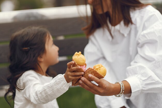 Familia en una ciudad. Niña come helado. Madre con hija sentada en un banco.