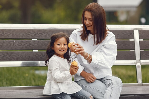 Familia en una ciudad. Niña come helado. Madre con hija sentada en un banco.