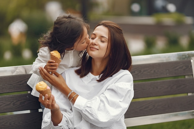 Familia en una ciudad. Niña come helado. Madre con hija sentada en un banco.