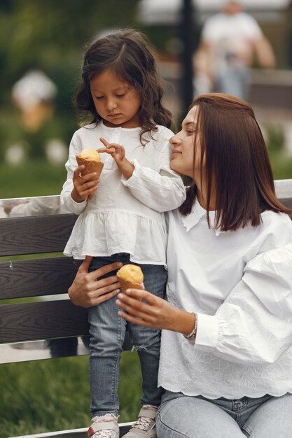 Familia en una ciudad. Niña come helado. Madre con hija sentada en un banco.