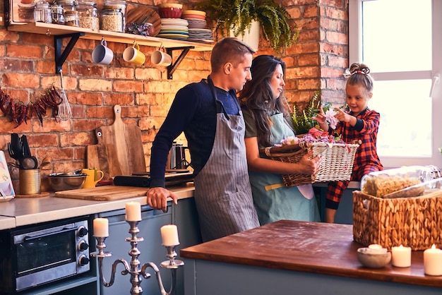 Familia en cocina estilo loft por la mañana. La madre sostiene una canasta con flores y habla con su pequeña hija.