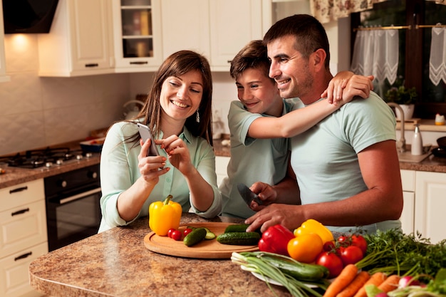 Foto gratuita familia en la cocina mirando fotos en el teléfono inteligente