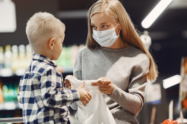 Familia comprando comestibles. Madre en suéter gris. Mujer con una máscara médica. Tema de coronavirus.