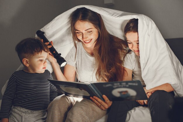 Familia debajo de la manta en la cama leyendo un libro.