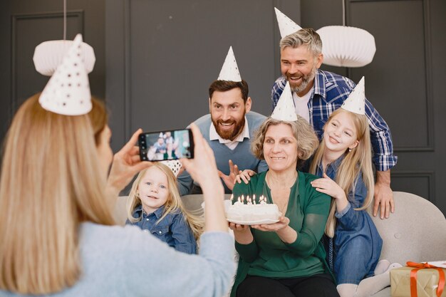 Familia y dos de sus hijas celebran cumpleaños Dos hombres y dos niñas sentados en un sofá La madre está tomando una foto de ellos