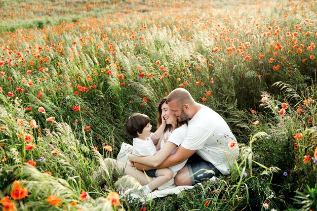 Familia encantadora diviértete sentado en el campo de amapolas