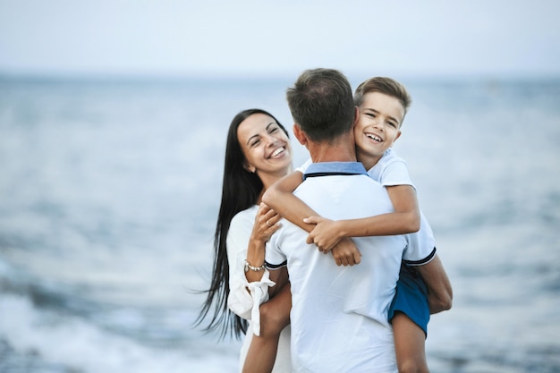 La familia está de pie en la orilla del mar y felizmente sonriendo, concepto de familia