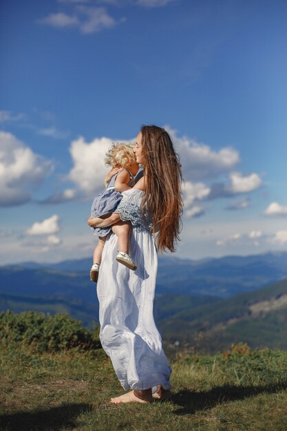 Familia con estilo en las montañas. Mamá e hija sobre un fondo de cielo. Mujer con un vestido blanco.