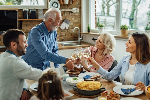 Familia extendida feliz disfrutando de un almuerzo y brindando con vino en la mesa de comedor