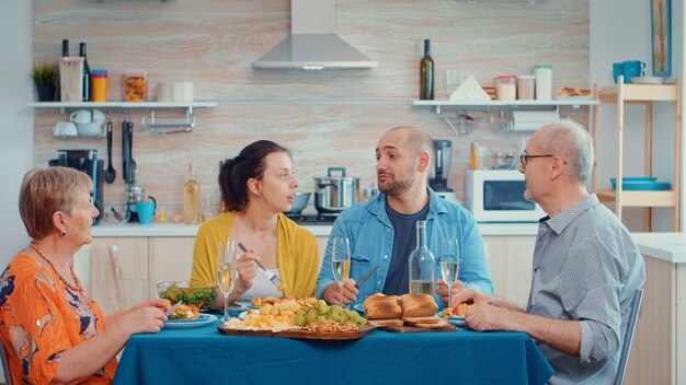 Familia extensa hablando con tiempo de relajación. Varias generaciones disfrutando del tiempo en casa, en la cocina sentados a la mesa, cenando juntos y bebiendo