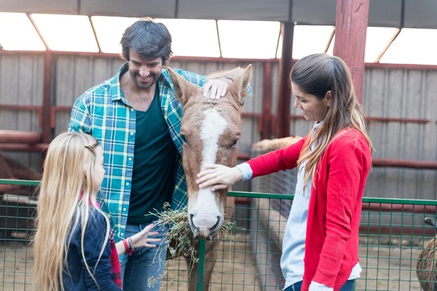 Familia feliz alimentando a un caballo en el establo