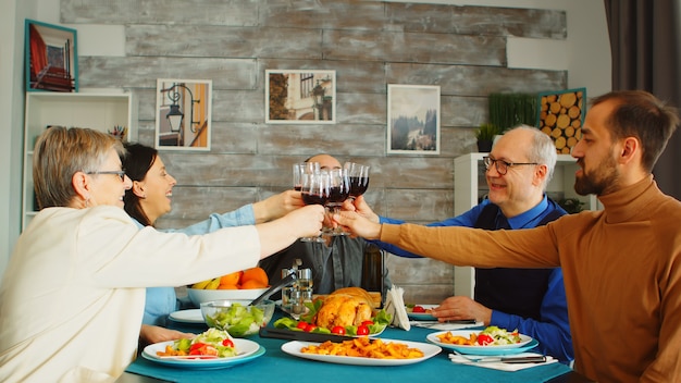 Familia feliz durante el almuerzo brindando con vino tinto. Amigos y familiares en la cena del domingo.