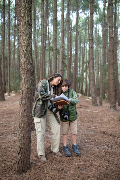 Familia feliz con cámaras caminando en el bosque. Madre e hijo de cabello oscuro con abrigos preparándose para tomar fotografías, discutiendo la ruta. Crianza, familia, concepto de ocio.