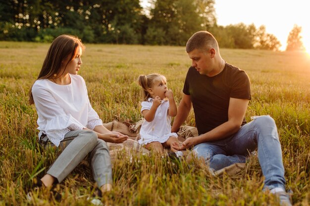 Familia feliz en un campo en otoño. Madre, padre y bebé juegan en la naturaleza bajo los rayos del sol