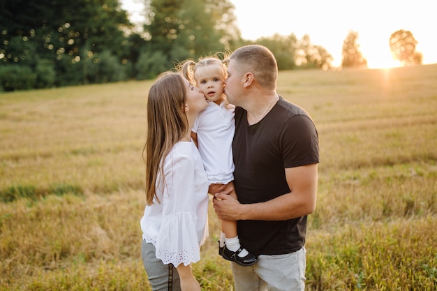 Familia feliz en un campo en otoño. Madre, padre y bebé juegan en la naturaleza bajo los rayos del sol