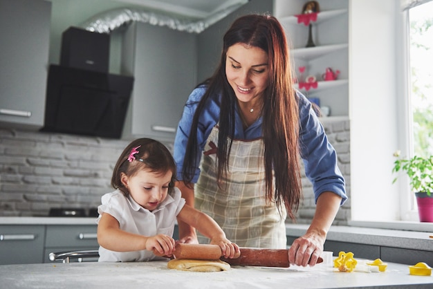 Familia feliz en la cocina. Concepto de comida de vacaciones. Madre e hija preparando la masa, hornear galletas. Familia feliz en hacer galletas en casa. Comida casera y pequeño ayudante