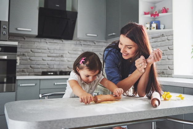 Familia feliz en la cocina. Concepto de comida de vacaciones. Madre e hija preparando la masa, hornear galletas. Familia feliz en hacer galletas en casa. Comida casera y pequeño ayudante