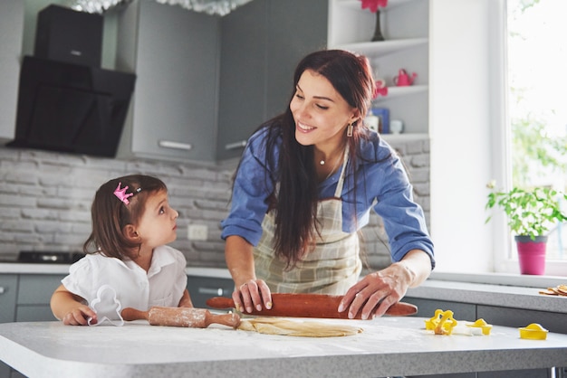 Familia feliz en la cocina. Concepto de comida de vacaciones. Madre e hija preparando la masa, hornear galletas. Familia feliz en hacer galletas en casa. Comida casera y pequeño ayudante