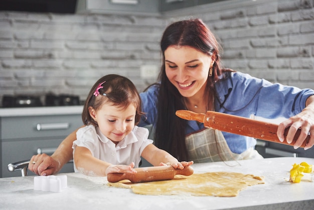 Foto gratuita familia feliz en la cocina. concepto de comida de vacaciones. madre e hija preparando la masa, hornear galletas. familia feliz en hacer galletas en casa. comida casera y pequeño ayudante