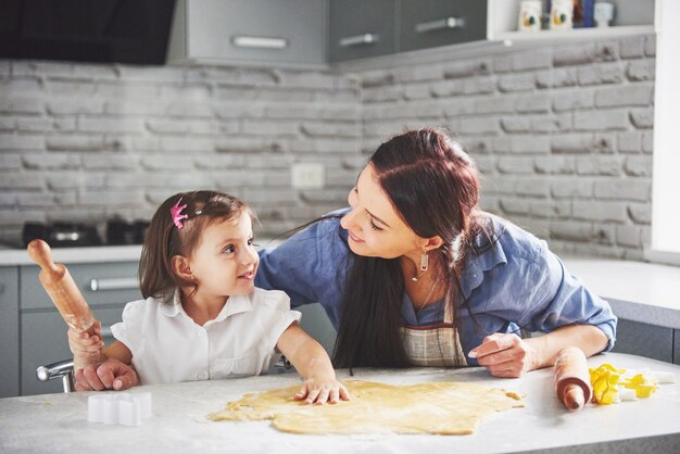 Familia feliz en la cocina. Concepto de comida de vacaciones. Madre e hija preparando la masa, hornear galletas. Familia feliz en hacer galletas en casa. Comida casera y pequeño ayudante