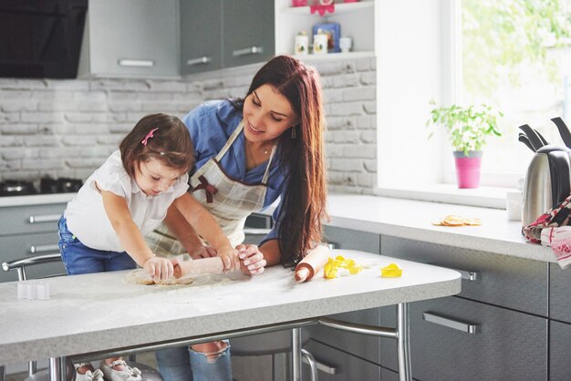 Familia feliz en la cocina. Concepto de comida de vacaciones. Madre e hija preparando la masa, hornear galletas. Familia feliz en hacer galletas en casa. Comida casera y pequeño ayudante