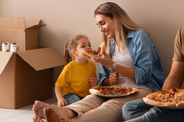 Familia feliz comiendo pizza en su nuevo hogar