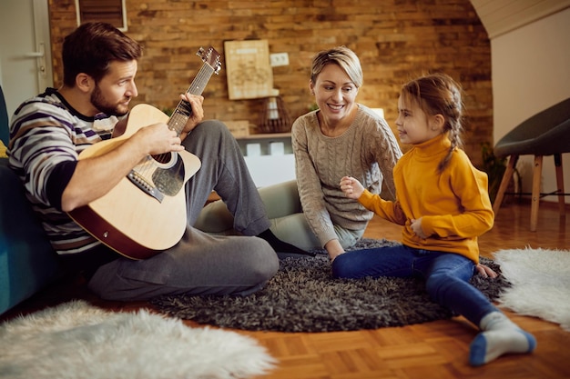 Familia feliz disfrutando mientras el padre toca la guitarra acústica en casa