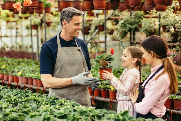 Familia feliz disfrutando mientras trabajan juntos en el vivero de plantas La niña sostiene una flor en maceta