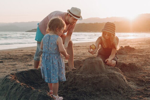 Familia feliz divirtiéndose juntos en la playa al atardecer. Construyendo castillo de arena
