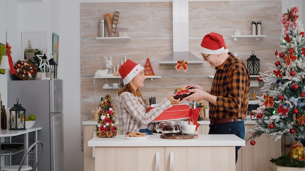 Familia feliz con envoltura de regalo de Navidad con cinta en la cocina decorada de Navidad