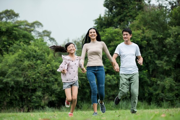 La familia feliz se está divirtiendo Madre, padre e hija se están ejecutando en el parque.