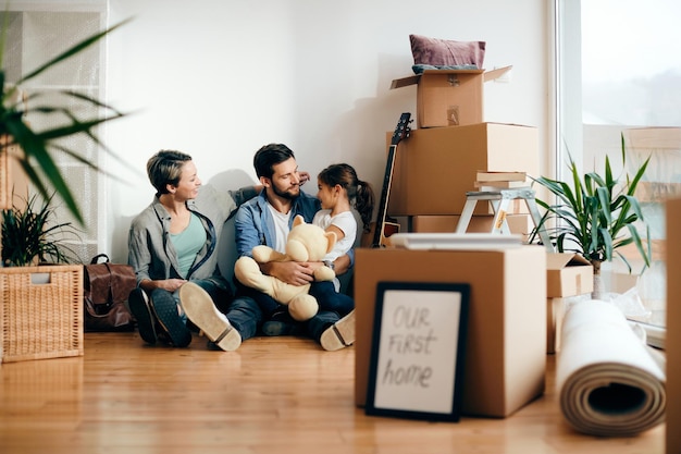 Familia feliz hablando mientras se relaja en el suelo en su nuevo hogar