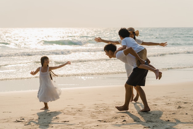 La familia feliz joven asiática disfruta de vacaciones en la playa en la noche. Papá, mamá y niño se relajan jugando juntos cerca del mar cuando se pone el sol mientras viajan de vacaciones. Concepto de estilo de vida viajes vacaciones vacaciones verano.