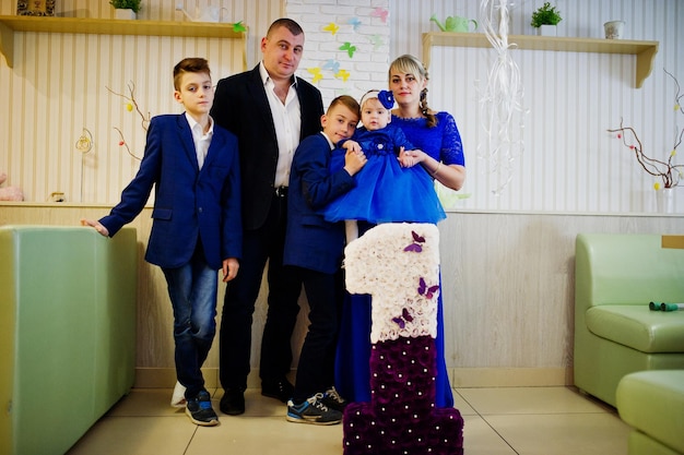 Familia feliz con una linda niñita en un vestido azul de 1 año de cumpleaños