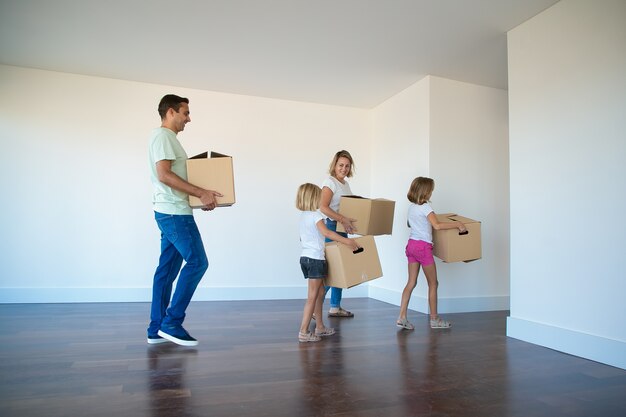 Familia feliz llevando cajas de cartón de la habitación vacía