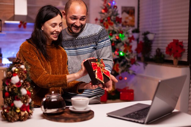 Familia feliz mostrando sorpresa de regalo de Navidad a amigos remotos durante una videollamada en línea