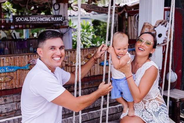 Familia feliz con un niño en columpio fuera del hotel