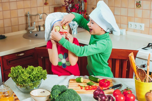 Familia feliz niños divertidos están preparando una ensalada de verduras frescas en la cocina