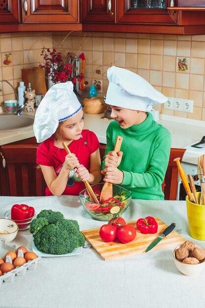 Familia feliz niños divertidos están preparando una ensalada de verduras frescas en la cocina