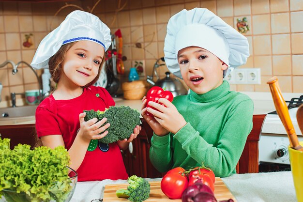familia feliz niños divertidos están preparando una ensalada de verduras frescas en la cocina