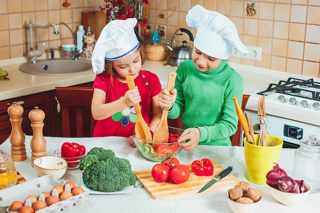 Familia feliz niños divertidos están preparando una ensalada de verduras frescas en la cocina