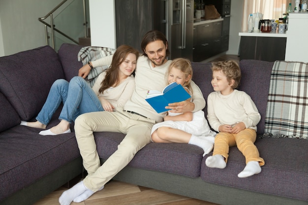 Familia feliz con los niños leyendo libro juntos sentados en el sofá