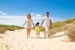 Foto gratuita familia feliz pareja y niño en ropa de verano caminando por el camino de arena blanca, niña cogidos de la mano de los padres